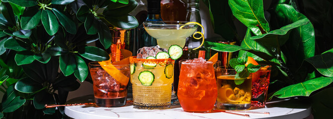 Spiced tequila old fashioned, alcoholic cocktail drink with tequila, soda, ice and lemon peel. Marble table in lounge bar with green plants