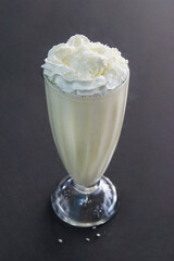 Milkshake in a tall glass with whipped cream and coconut chips
