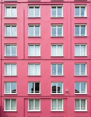 Fototapeta premium Pink building facade with numerous windows. A vibrant and symmetrical architectural detail, showcasing a consistent design pattern.