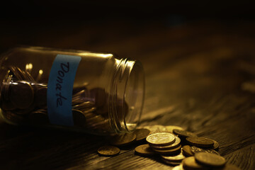 Donation Jar with Coins on Wooden Table in Dim Light, Symbolizing Charity and Giving