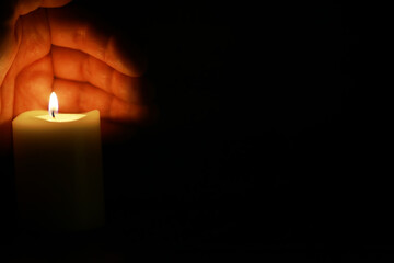 Hand Hovering Over Lit Candle in Darkness, Symbolizing Warmth and Protection