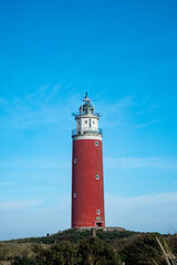 Eierland, De Cocksdorp, Texel, The Netherlands, Oktober 28th, 2024, A stunning vertical photo features a red lighthouse against a vibrant blue sky, surrounded by nature