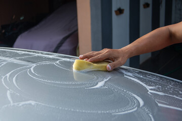 Washing car at home : people spraying foamy car shampoo with pressure sprayer, outdoor environment
