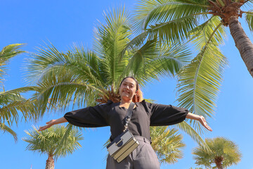 Low angle view. happy asian woman on the coconut tree blue sky background. Travel Rayong Province, Thailand.