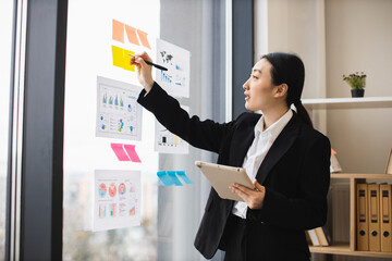 Asian businesswoman holding tablet presenting data analysis. Office setting with charts on glass...