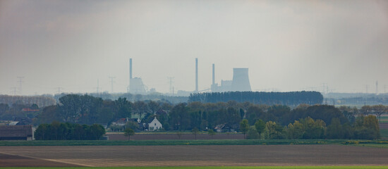 Fototapeta premium View of a hazy landscape featuring distant industrial structures and a serene countryside in late autumn