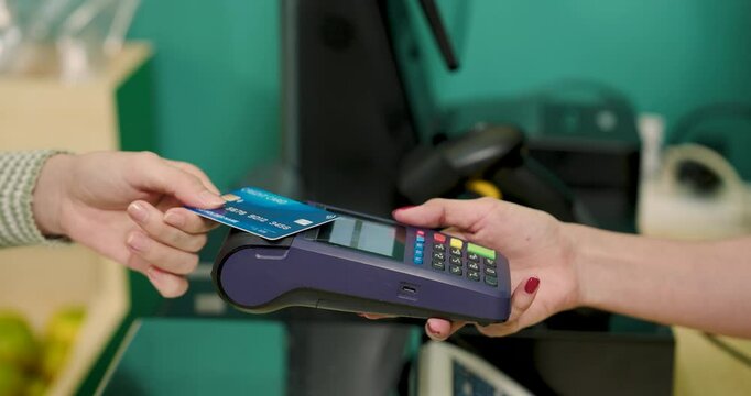 Contactless credit card payment being processed in small fruit shop. Customer holding credit card, while cashier operates payment terminal. modern transaction methods in local businesses.