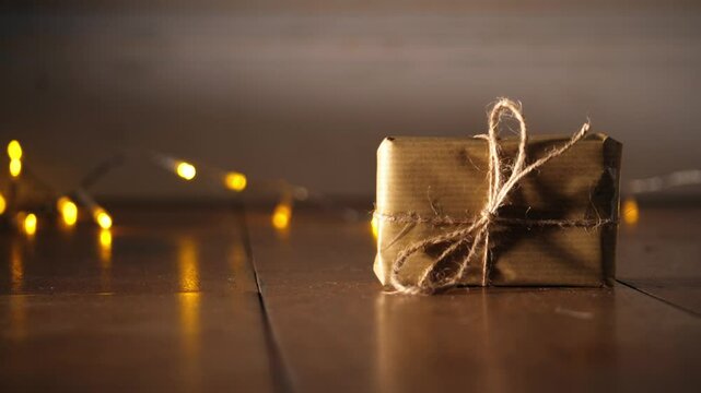 Gift wrapped in brown paper and string with Christmas lights bokeh background