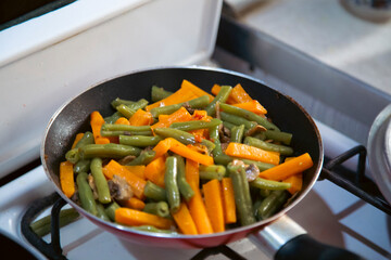 Frying fresh vegetables including carrots, mushrooms and green beans in a pan. 