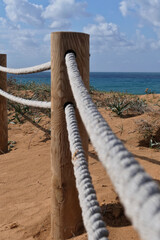 Obraz premium Rope fence on the beach with blue sky and sea in background in Netanya. Sturdy rope fence, composed of thick, grey ropes secured between light brown wooden posts