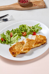Crispy Chicken Fillet with Cheese Crust and Fresh Salad on Elegant White Plate