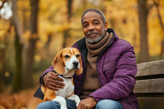 Senior African American man sitting on a park bench with his Beagle dog during a peaceful autumn day, surrounded by golden foliage and enjoying the outdoors.