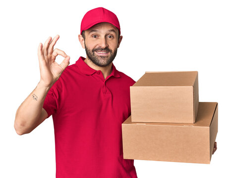Hispanic male courier with boxes cheerful and confident showing ok gesture.
