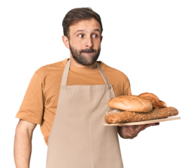 Hispanic male baker with bread tray confused, feels doubtful and unsure.