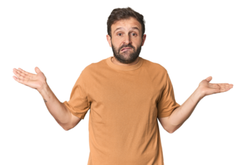 Studio portrait of young Hispanic male confused and doubtful shrugging shoulders to hold a copy space.