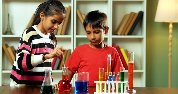 Indian Asian Curious Cute Little Girl and Boy Siblings Playfully Exploring Science Using Chemicals, Glass Beakers, and Test Tubes for Fun Experiments While Sitting at Table in Classroom