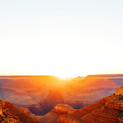 Naklejka premium Stunning sunrise over the majestic Grand Canyon, showcasing vibrant colors across rugged terrains and a clear blue sky.