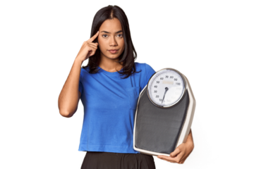 Filipino woman with scale in studio pointing temple with finger, thinking, focused on a task.