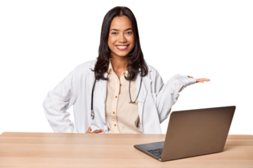 Young Filipino doctor with laptop in studio showing a copy space on a palm and holding another hand on waist.