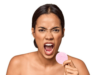 Woman holds facial sponge in studio screaming very angry and aggressive.