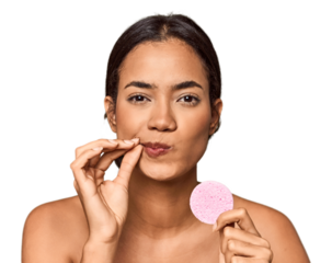 Woman holds facial sponge in studio with fingers on lips keeping a secret.