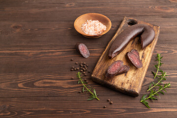 Sujuk sausage on wooden cutting board with pepper and herbs on brown wooden. Side view, copy space.