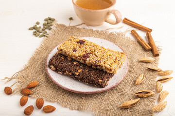 granola bars with caramel, nuts, flakes in ceramic plate on white wooden. Side view, close up.
