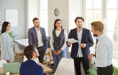 A group of six professionals engaged in a discussion during a meeting in a contemporary office. Two...