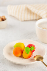 Marzipan candies in the form of fruits: pear, tangerine, lemon and strawberry in a plate with a cup of coffee. Vertical orientation.