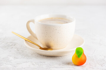 Cup of cappuccino coffee with a marzipan candy in the form of a pear on the table.