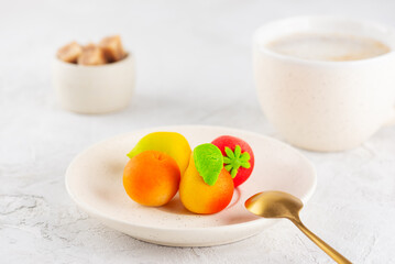 Marzipan candies in the form of fruits in a plate with a cup of coffee.