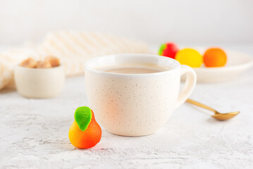 A cup of cappuccino coffee with marzipan candies in the form of fruits on the light table. Sweet dessert, breakfast.