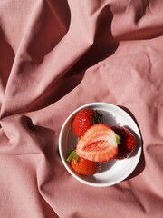 Fresh Strawberries in a White Bowl on a Pink Fabric Background