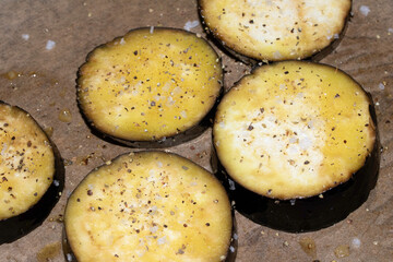 A seasoned sliced aubergine eggplant with salt and herbs waiting to be cooked in the oven close up raw