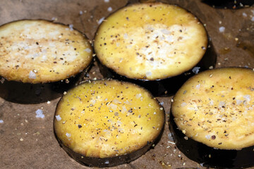 A seasoned sliced aubergine eggplant with salt and herbs waiting to be cooked in the oven close up raw