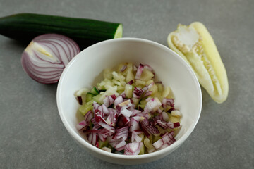 A white bowl filled with a mix of diced red onion, cucumber, and Hungarian wax pepper.