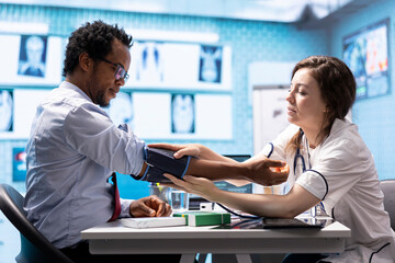 Fototapeta premium Physician measuring pulse and controlling blood pressure for a patient, using blood pressure monitor during check up visit. Doing a consultation on health insurance, medical services.
