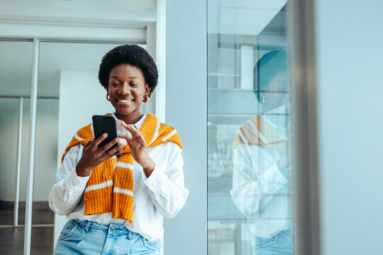 Confident female architect dressed casually with orange sweater using smartphone