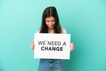 Young caucasian woman isolated on blue background holding a placard with text We Need a Change