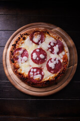 Pizza with salami and mozzarella cheese. Wooden background. Soft focus. Top view. Copy space.