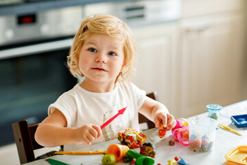 Adorable cute little toddler girl with colorful clay at home. Healthy baby playing and creating toys from play dough at nursery or playschool. Small kid molding modeling clay, creative activity