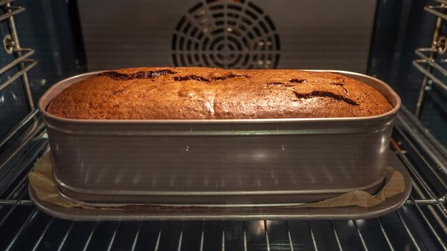 Time-lapse of a homemade chocolate loaf cake rising and baking in an oven. The raw batter transforms into a baked dessert with a cracked top in a rectangular pan, showcasing the cooking process.
