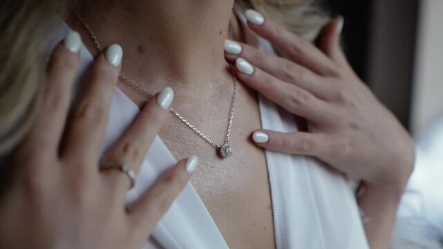 a beautiful young bride in a white dress with an open neckline hangs pearl jewelry on her neck and strokes her body, morning preparations before the wedding ceremony