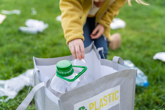 Unrecognizable kittle girl picking up plastic bottles