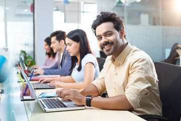 Smiling Office Companion Looking At Camera While Working On Laptop In Office