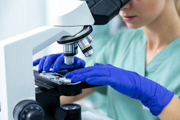 Medical woman in laboratory studying samples under microscope with protective gloves