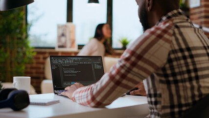 African american software engineer works on a laptop typing code for a development project....
