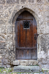 Fototapeta premium An ancient wooden door with iron reinforcements and a small window, set within a stone wall of a medieval castle, reflecting timeless craftsmanship and historical charm.
