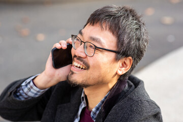 Close-up of smiling Asian man talking on smartphone