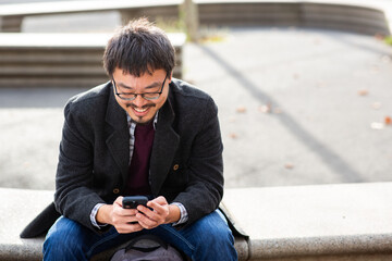 Asiatic man smiling while using phone outdoors
